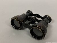 Side angled view showing the textured black body, brass accents on lenses, and central focusing wheel of the opera glasses.