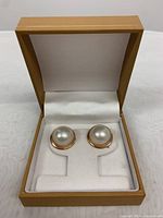 Pair of pearl earrings set in 14K gold displayed in an open jewelry box with white velvet padding.