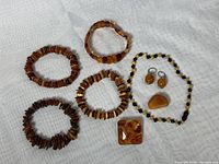 Overview photo showing all amber jewelry items in the lot on a white textured background, including necklace, earrings, brooch, and multiple bracelets.