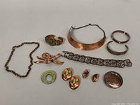 Full lot view showing various copper jewelry including cuff, rings, brooches, bracelets, and earrings arranged on white background.
