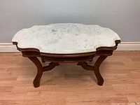 Front view of vintage coffee table showing marble top and wooden base with curved legs.