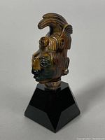 Side view of a carved Tigers Eye stone head sculpture of King Pakal the Great, mounted on black Onyx pedestal with silver earrings and headdress details.