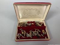 Opened box containing assorted vintage men's cufflinks, tie clips, and pins in a red velvet-lined case labeled MELE.
