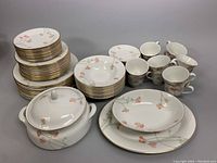 Photo showing stacks of dinnerware plates, bowls, and covered serving bowl with floral pattern and gold rims.