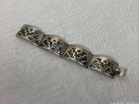 Full view of the linked abalone shell and silver panel bangle bracelet laid out flat on a textured fabric background.