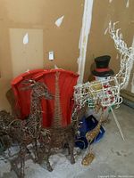 Photo showing two wicker wire reindeer in front of the red plastic sleighs, white wire reindeer, and blue plastic slide shovel in garage corner