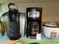 Front view showing all three appliances on table: Keurig coffee maker, Cuisinart coffee maker, and Black & Decker rice cooker.