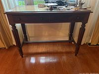 Full view of the wooden console table showing two drawers and fluted legs on hardwood floor near window.