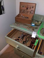 Wooden box with jewelry compartments, displayed on a table with drawer open showing more necklaces inside and bracelets on top of the drawer.