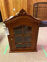 Front view of the wood hanging curio cabinet showing carved top and six-pane glass door.