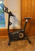 Side view of stationary bike showing frame, seat, and pedals.