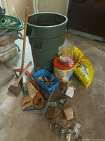 Overall lot with garbage pails, bird seed bag, vintage canister, and small bins of hardware on floor close to wall