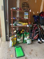 Overview of garden supplies on shelving unit and floor including fertilizer bags, sprinklers, hand tools, gloves, and decorative stakes