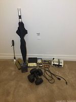 Full lot overview against a beige carpeted wall includes umbrella, shoehorn, hairbrush, cufflinks, dominoes, dumbbells, alarm clock, perfume, bowtie, money clip.