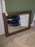 Full view of the large rectangular mirror leaning against a wall showing the full frame and beveled glass.