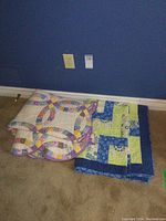 Both quilts folded and stacked on beige carpet against blue wall