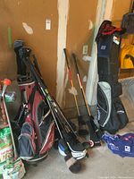 Red and black TaylorMade golf bag and black Callaway golf bag with clubs and covers against garage wall