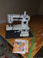 Front angled view of white Kenmore sewing machine model 1340 with foot pedal and instruction manual on table.