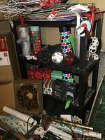 Black resin shelving unit shown fully loaded with miscellaneous holiday-themed wrapping items, gift boxes, and decorations.