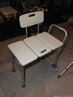 Front angle showing aluminum frame, white plastic seat with drainage holes, backrest with handle cut-out and one armrest.