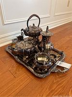 Photo showing full silver plated tea set on the tray including teapot, coffee pot, creamer, sugar bowl, warmer, and strainer with ornately detailed tray and heavy tarnish.