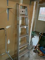 Full view of the aluminum 6 ft step ladder standing in a garage, showing the overall structure and condition.