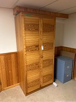 Front view of wood cabinet with two closed paneled doors and round wood knob handles set against wood-paneled basement wall