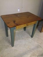 Full view of the solid wood table showing drawer and painted legs.