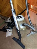 Electrolux Ultrasilencer Deluxe vacuum with attached hose and floor tool. Various black attachments visible in background along with vacuum bags.