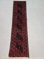 Full view of the Persian Balouch wool runner rug showing the red geometric design on black background.