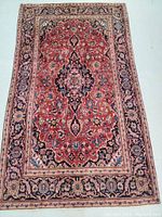 Full view of the Persian Kashan rug showing the detailed floral pattern and central medallion design with predominant red and navy colors.