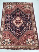 Full view of the Persian Shiraz rug showing central blue medallion on a red and cream background with intricate tribal patterns.