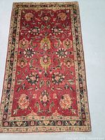 Full view of the hand knotted Persian Tabriz wool rug showing floral all-over pattern with cream border on red background.