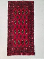 Full view of the rectangular Turkmen wool rug showcasing its red field with geometric motifs and multiple borders.