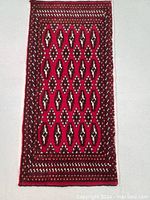 Full view of the rectangular hand knotted Turkmen wool rug with red background and geometric patterns