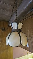 Side angle view of vintage swag glass lamp hanging from ceiling chain with wooden panel background.