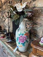 Full view of porcelain vase decorated with colorful flowers and birds, holding faux flowers on a stone surface.