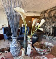 Lot of Asian and Lenox style vases and floral bowl arranged on table with artificial flowers inside some vases and surrounding decor.