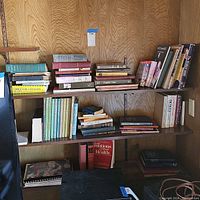 Wide shot showing multiple shelves filled with books of various sizes and colors, many vintage and hardcover, arranged standing and stacked.