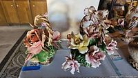 Both Capodimonte porcelain floral baskets displayed on a table, showing woven basket handles and detailed flowers.