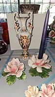 Tall ornate Capodimonte porcelain urn with cherub and floral decoration, two pink rose-shaped porcelain floral candlesticks, one holding a purple candle.