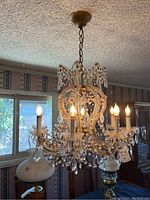 Chandelier lit up showing six light bulbs and crystal bead decoration hanging from a golden chain attached to ceiling.