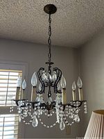 Front side view of the metal and crystal chandelier hanging from the ceiling with six candle-shaped bulbs and multiple hanging crystal beads and pendants.