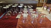 Photo showing a group of 28 crystal stemware glasses arranged upside down and upright on a red cloth.