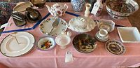 Wide view showing multiple items: floral teapot, serving dishes, salt & pepper shakers, and collector plates on a pink tablecloth.