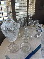 Wide view showing large etched crystal candy dish with lid, multiple decanters, and some barware items on table near window