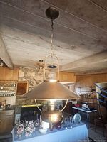 Wide shot of hanging lantern lamp in rustic setting showing metal conical shade, chain, and ceiling mount