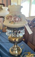 Front view of electric hurricane lamp showing floral painted glass shade with pink roses, brass base, and hanging crystal prisms.
