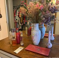 Wide view of all items on wooden dresser surface with mirror behind showing perfume bottles, vases with dried flowers, and trinket dish.