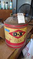 Front and partial side view of the vintage D-X motor oil can showing the logo and the condition of the metal can with rust and paint wear.